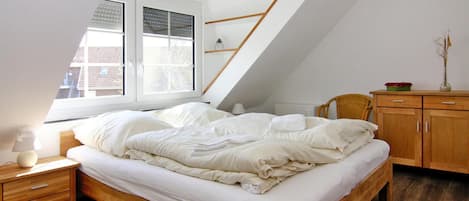 A bedroom with a sloped ceiling, a wooden bed, a nightstand, a chair, a dresser, and a window with blinds.