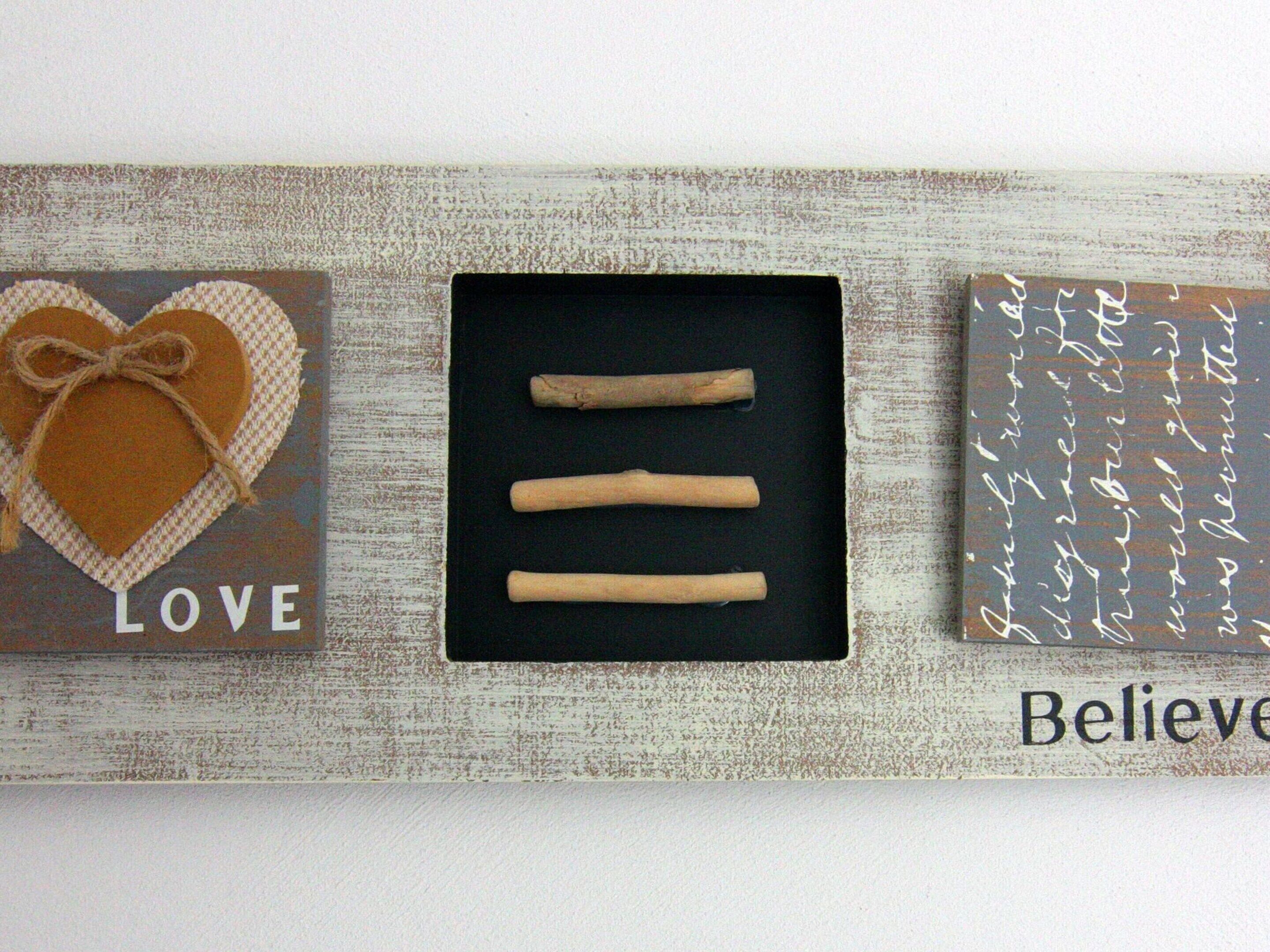 Three decorative items: a heart with 'LOVE' on a textured background, a black box with three sticks, and a sign with 'Believe' and cursive writing.