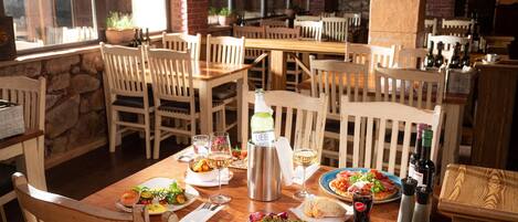 Un restaurante con mesas y sillas de madera, varios platos, copas de vino y botellas.