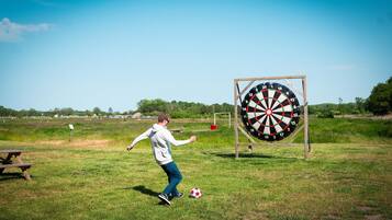 Una persona juega al fútbol en un campo cubierto de hierba, con un dardo en el fondo.