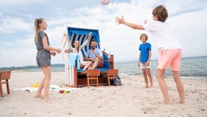 Una spiaggia con una sedia a sdraio e un tavolo, una persona seduta e un'altra in piedi nelle vicinanze.