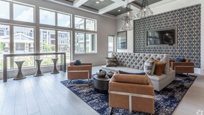 Un salon spacieux avec une grande fenêtre, un canapé gris et un mur orné d’un motif.