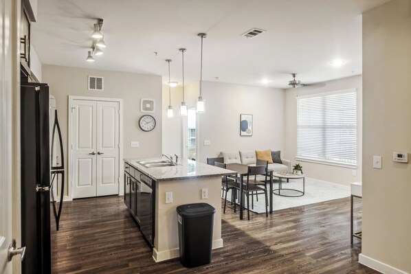 A modern kitchen with a central island, a dining area with a table and chairs, and a living room with a sofa and a coffee table.