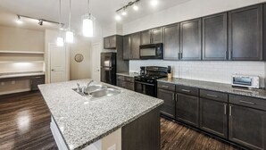 Une cuisine moderne avec des meubles de couleur sombre, des plans de travail en granit, des appareils électroménagers en acier inoxydable et des luminaires suspendus.