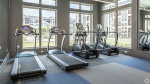 Uma academia com esteiras e aparelhos elípticos, grandes janelas e vista para edifícios residenciais.