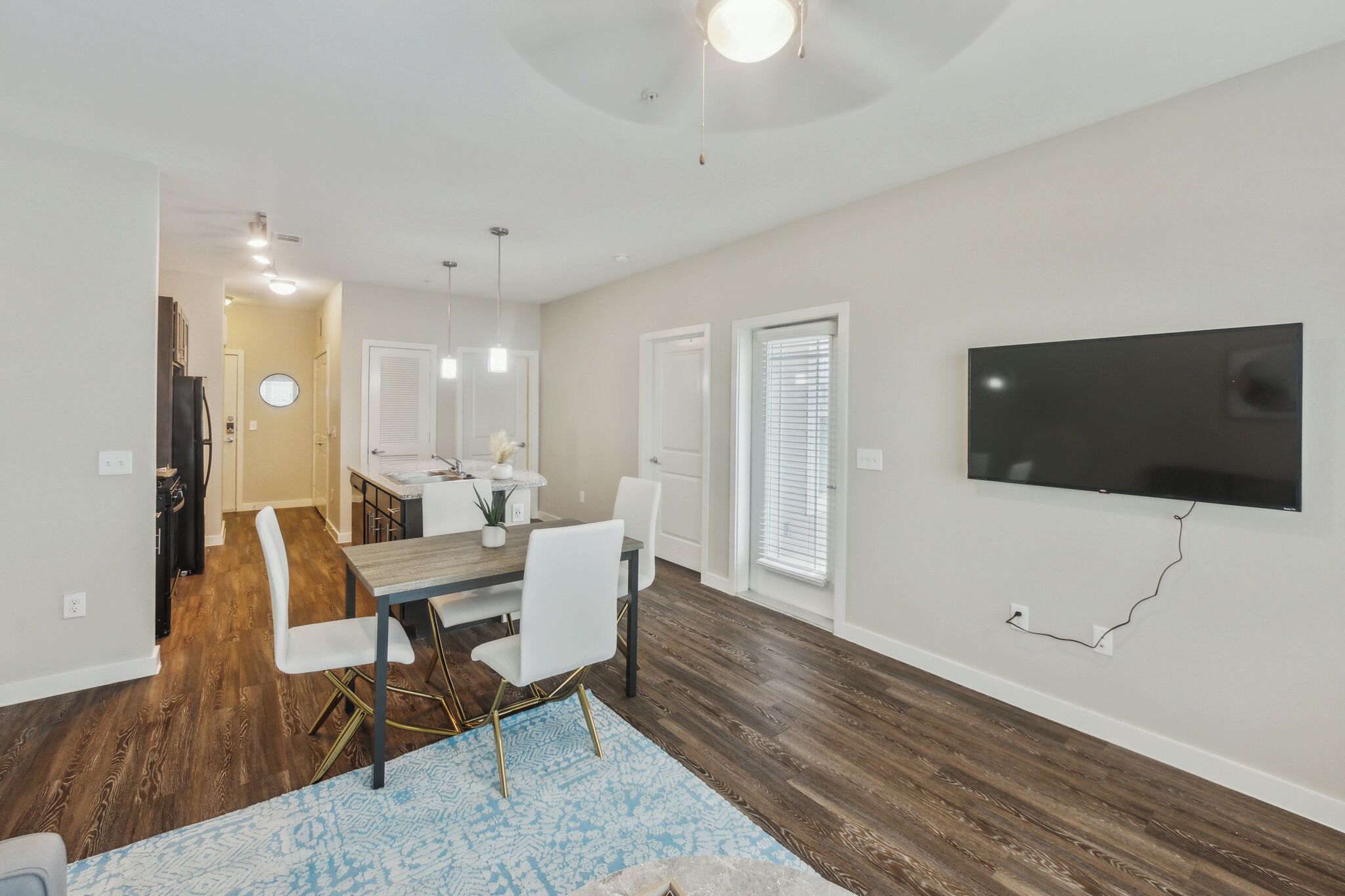 A modern living room with a dining area, a flat-screen TV mounted on the wall, and hardwood flooring.