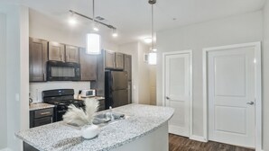 A modern kitchen with granite countertops, stainless steel appliances, and pendant lighting.