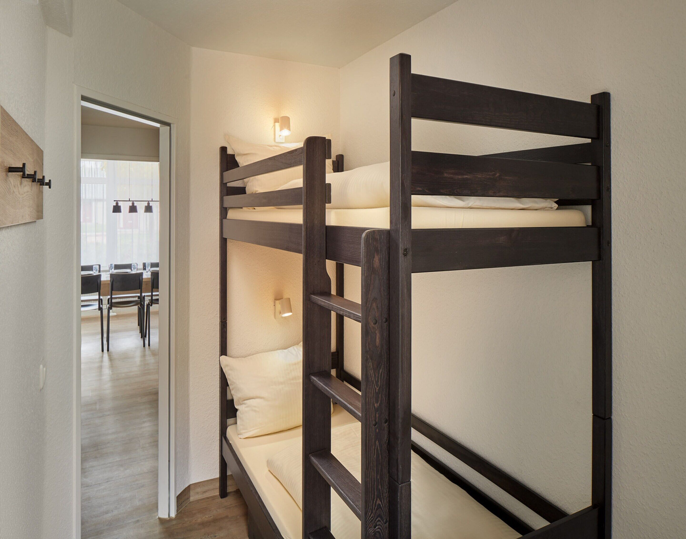 A bunk bed with a wooden frame, a small table with chairs, and a wall-mounted light fixture.
