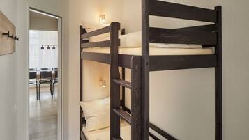 A bunk bed with a wooden frame, a small table with chairs, and a wall-mounted light fixture.