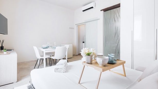 Una habitación de hotel moderna con una cama, un área de comedor con mesa y sillas, una pequeña cocina y un espejo grande.