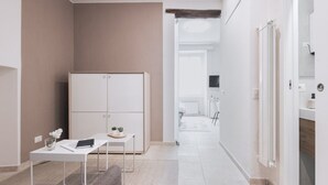 Una habitación de hotel moderna y minimalista, con una paleta de colores neutros, un armario blanco, una pequeña mesa con una computadora portátil y una planta, y vistas al baño.