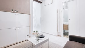 Una habitación moderna y minimalista con un armario blanco, una mesita con un florero y una libreta, y una puerta que da a un baño.