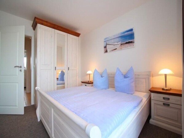 Une chambre à coucher avec un lit, deux tables de chevet avec des lampes, une porte et un tableau au mur.