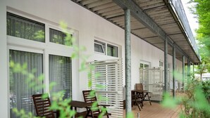 Une terrasse extérieure couverte, aménagée avec des meubles en bois et dotée de grandes fenêtres.