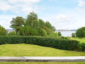 Une zone herbeuse, délimitée par une clôture en bois, d’où l’on peut admirer un plan d’eau et un paysage lointain.