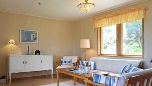 Un accogliente soggiorno con un divano, un tavolino in legno, un armadietto bianco, un lampadario e una finestra con tende.