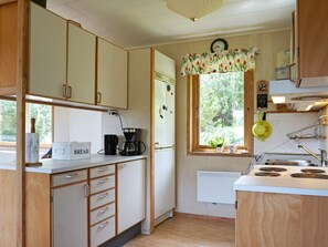 A compact kitchen with wooden cabinets, a coffee maker, a refrigerator, and a window with a view of greenery. - 6 Person Holiday Home in Kungshamn (Kungshamn)