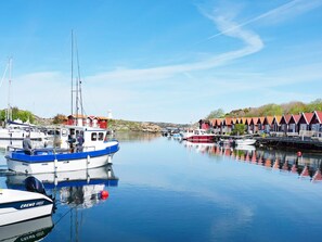 A marina with boats docked, a lighthouse in the background, and a row of red-roofed buildings. - 6 Person Holiday Home in Kungshamn (Kungshamn)