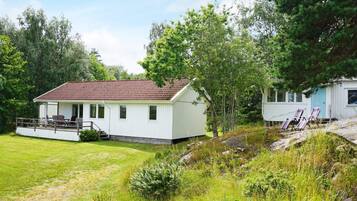 A white building with a red-tiled roof, a porch with chairs, and a grassy yard.