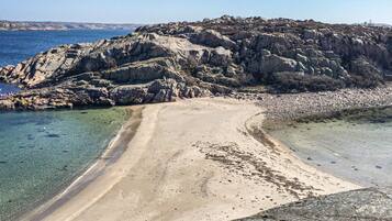 A coastal landscape with a sandy beach, clear water, and rocky terrain.