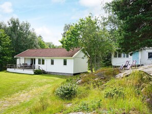 A white cabin with a red-tiled roof, a porch with chairs, and a grassy yard. - 6 Person Holiday Home in Kungshamn (Kungshamn)