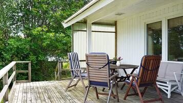 A wooden deck with outdoor furniture, including chairs and a table, and a white building with windows.
