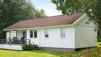 A white building with a tiled roof, a porch with chairs, and a grassy yard.