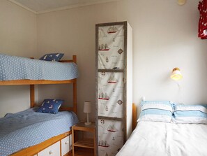 Habitación con literas, una estantería alta en la pared, una mesita de noche con lámpara, y una cama individual con almohadas a juego.