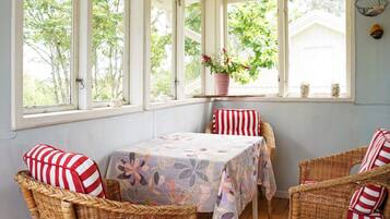 A room with a table and wicker chairs, large windows with a view of trees, and a hanging light fixture.