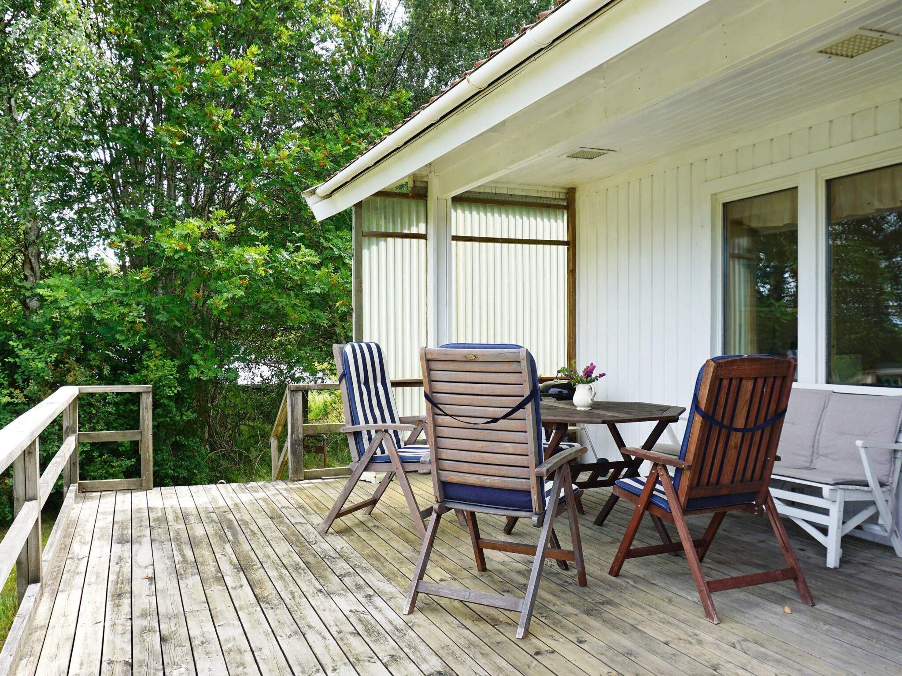 A wooden deck with outdoor furniture, including chairs and a table, and a white building with windows.