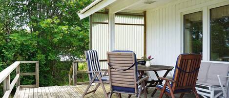 A wooden deck with outdoor furniture, including chairs and a table, and a white building with windows.