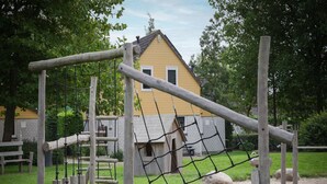 A playground with wooden structures and a netted climbing area. - Holiday Home in Zeeland With Garden Terrace (Wemeldinge)