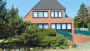 Une maison à deux étages, construite en briques, avec un toit à pignon, de nombreuses fenêtres et un petit jardin à l’avant.