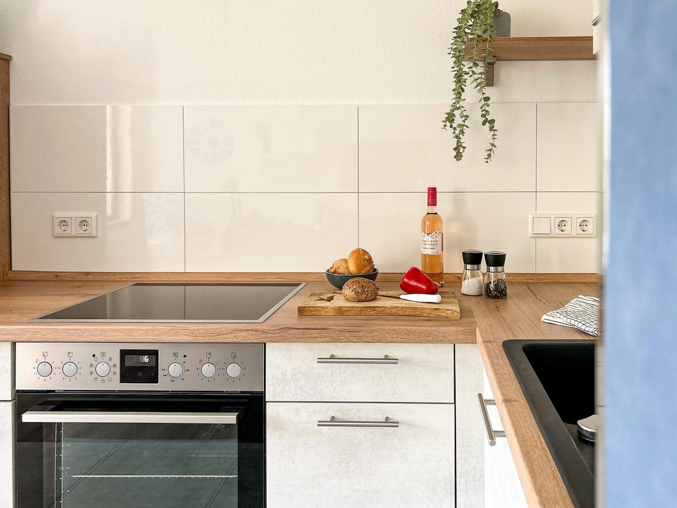 Une cuisine moderne avec des meubles blancs, un four encastré, un évier en acier inoxydable et un plan de travail en bois.