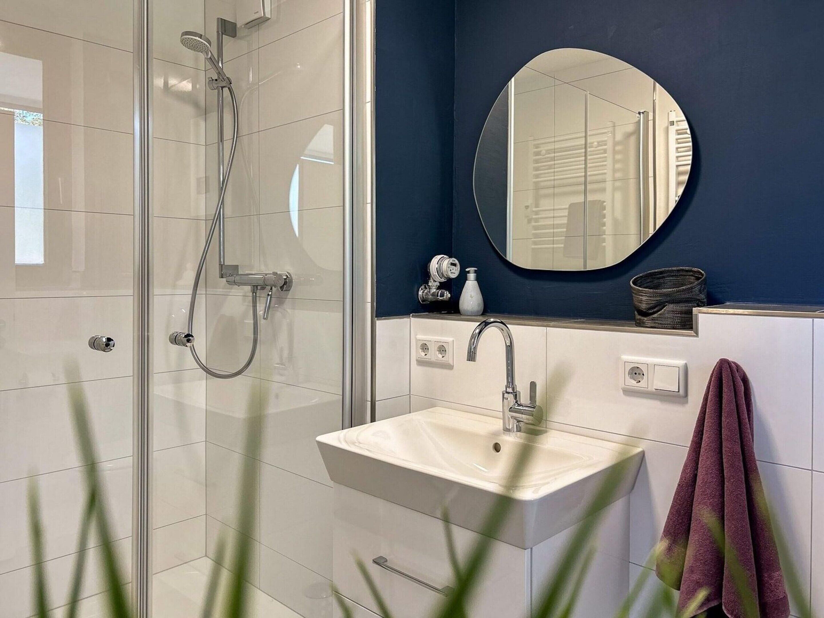 Un bagno moderno con cabina doccia in vetro, un lavandino bianco e uno specchio rotondo sopra.
