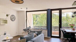 Una sala de estar moderna con un sofá gris, una silla colgante, una mesa de comedor con sillas y un ventanal con vistas a zonas verdes.