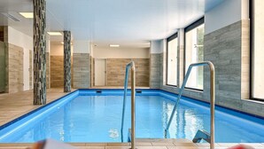 Una piscina interior con agua azul cristalina, rodeada de paredes de azulejos y grandes ventanales.