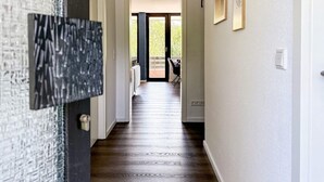 Un pasillo con suelo de madera, una puerta con panel de vidrio texturizado y vistas a un patio exterior con mesa y sillas.