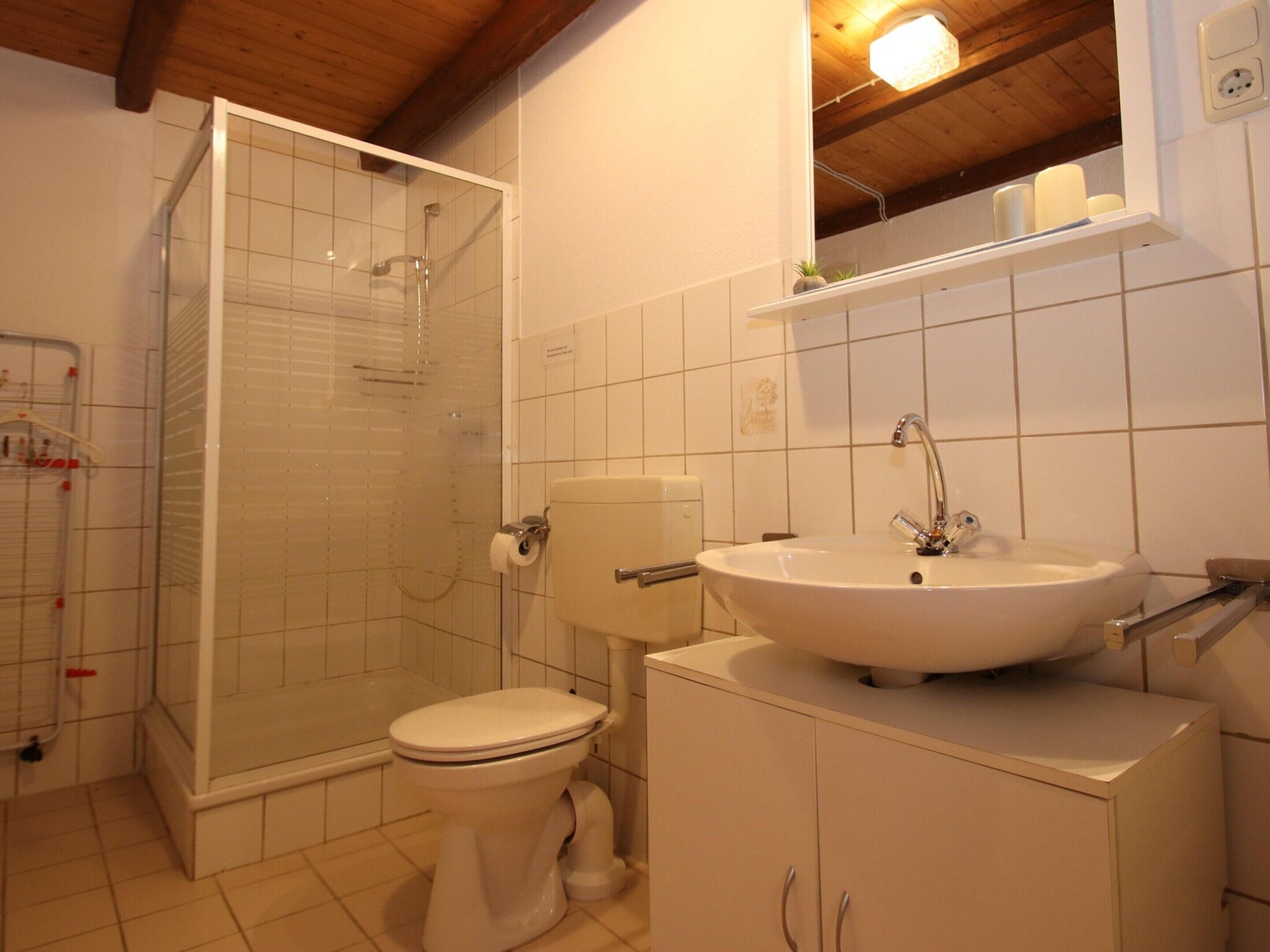 A bathroom with a glass-enclosed shower, a toilet, and a sink with a mirror above it.