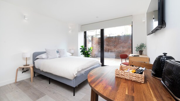 Ein modernes Schlafzimmer mit Bett, Nachttisch, Lampe und einem Essbereich mit Tisch und Stühlen.