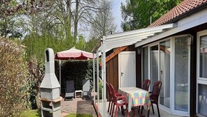 A patio with a grill, outdoor seating, and a covered area with a red umbrella. - Ferienhaus im Skandinavischen Stil (Mirow)