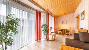 A spacious room with wooden flooring, a dining area with a table and chairs, and large windows with sheer curtains. - Ferienhaus im Skandinavischen Stil (Mirow)