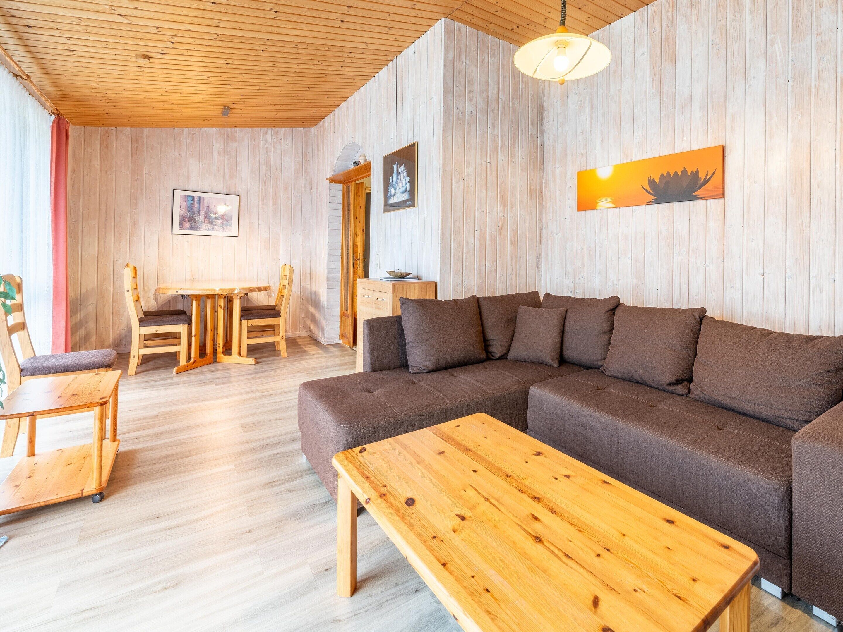 Ein gemütliches Zimmer mit Holzbalkendecke, einem braunen Sofa, einem Holztisch und einem Essbereich mit Stühlen und Tisch.
