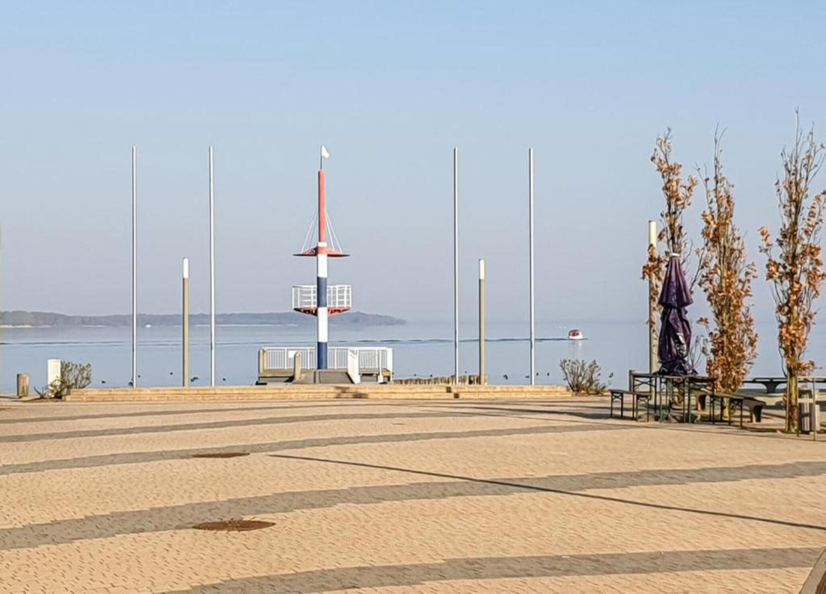 A waterfront promenade with a lighthouse, benches, and a clear view of the sea.