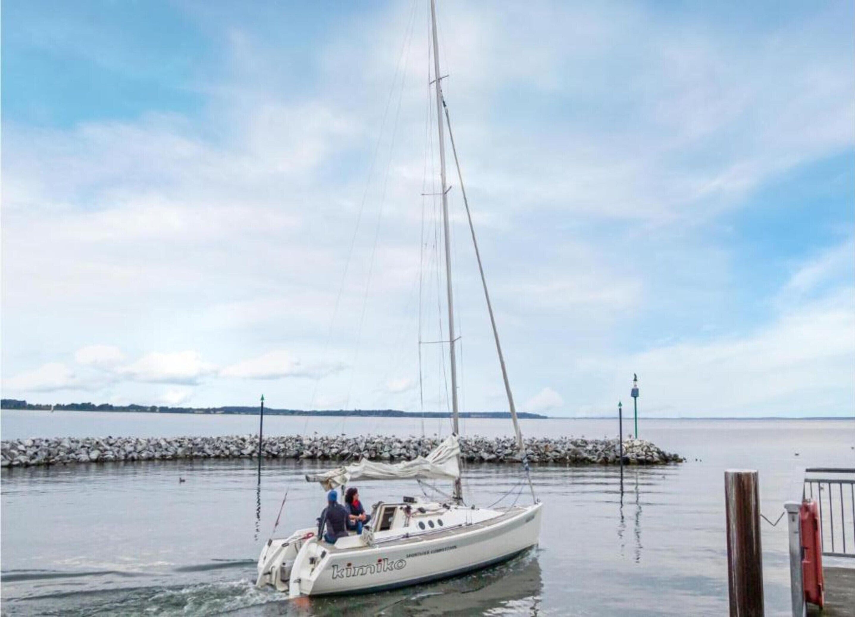 Un velero con dos personas a bordo, amarrado cerca de una costa rocosa.