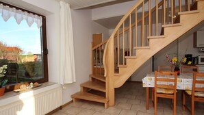 Una cocina con una escalera de madera, una mesa de comedor con sillas y un ventanal con cortinas.
