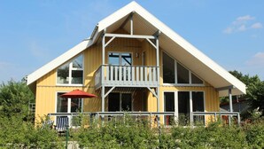 Ein zweistöckiges Holzhaus mit Balkon, großen Fenstern und einem roten Sonnenschirm.