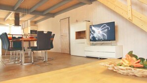 Eine moderne Küche mit Essbereich, Holzbalkendecke und einem Fernseher auf einem weißen Schrank.
