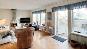 A cozy living room with a fireplace, comfortable seating, and large windows offering a view of the street. - 4 Star Holiday Home in Kallo-knippla (Källö-Knippla)