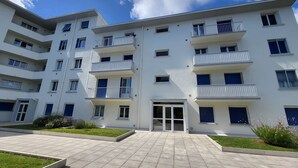 Un edificio residencial de varios pisos con balcones, una entrada central y un patio empedrado.
